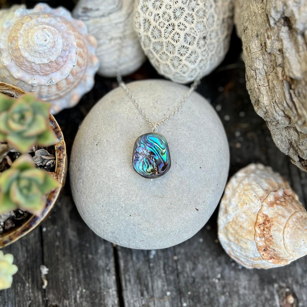 "Coastal Treasures" is a necklace that celebrates the raw and untamed beauty of nature. At its heart, it features a rustic abalone piece, measuring approximately 1 to 1.5 inches, hanging gracefully from a sterling silver chain.