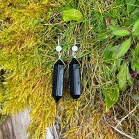 The Obsidian Shield Earrings are a striking pair of earrings that feature two polished Obsidian stones. Obsidian is a naturally occurring volcanic glass that is known for its protective properties. It is believed to shield against negative energy, providing a sense of safety and security.