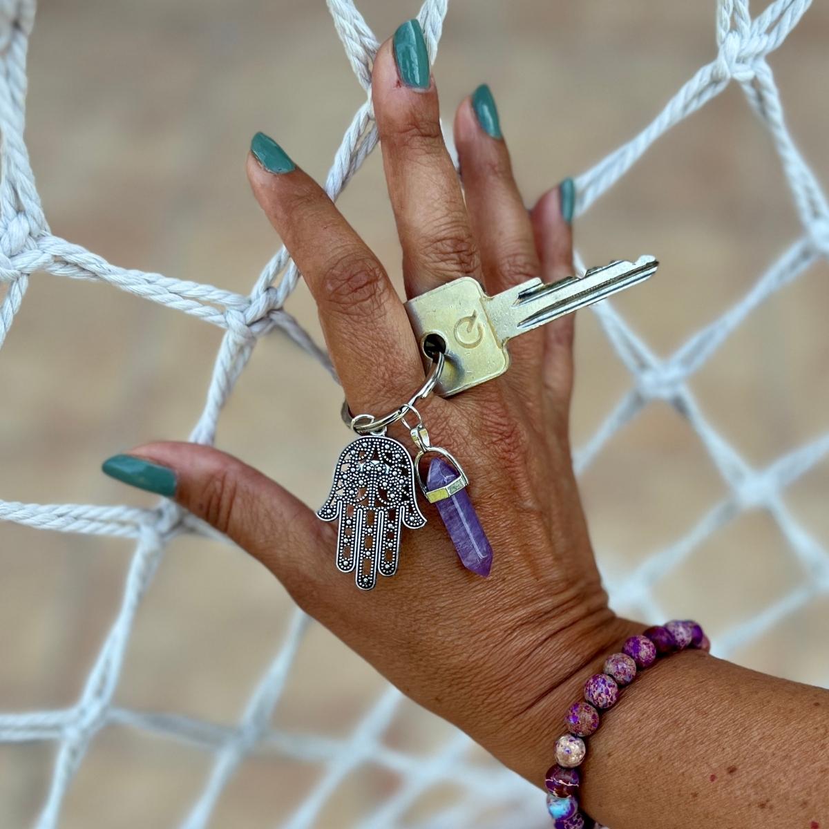 The "Hamsa - Shielding Hand Keychain" takes on a new enchanting form with the addition of a double-pointed Amethyst crystal and a dangling Hamsa hand charm. This keychain seamlessly blends spiritual significance with a touch of whimsy, creating a truly captivating accessory.
